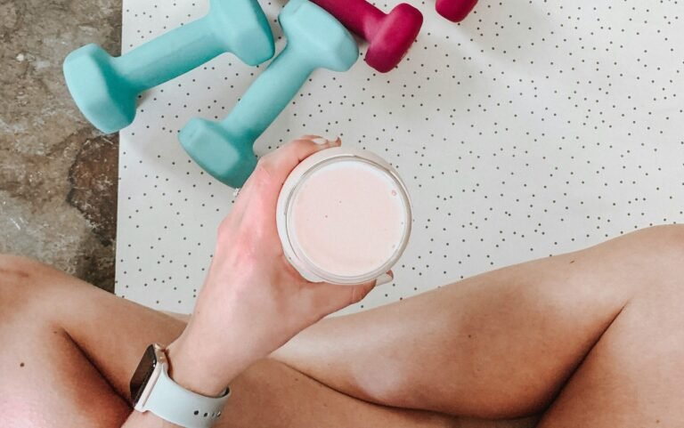 person holding white liquid filled cup above two pairs of dumbbells